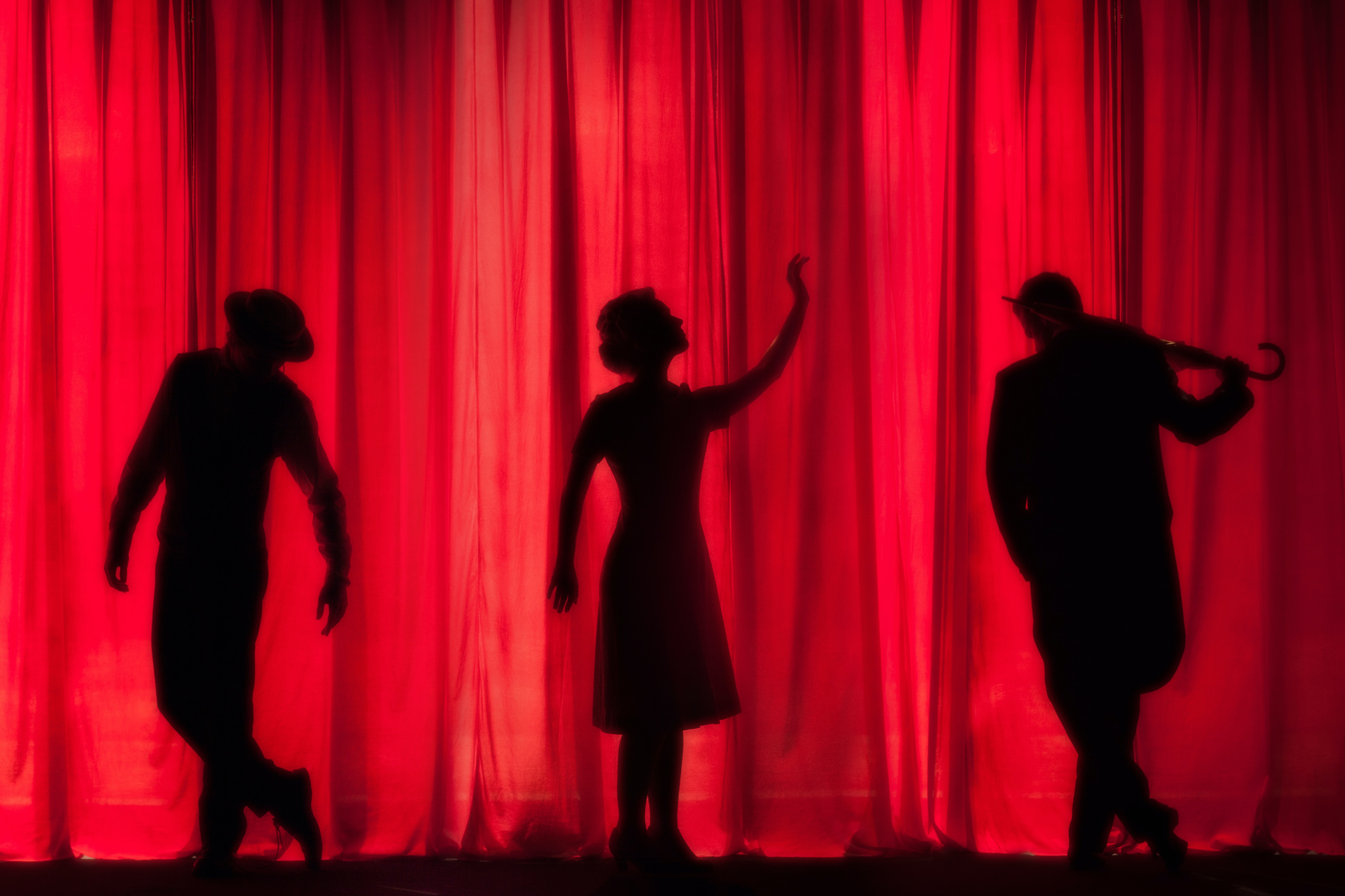 drei Silhouetten von Schauspielern vor einem roten Bühnenvorhang