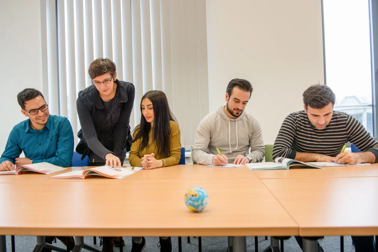 vier geflüchtete Studierende werden beim Lernen bei einer Lehrenden unterstutzt 