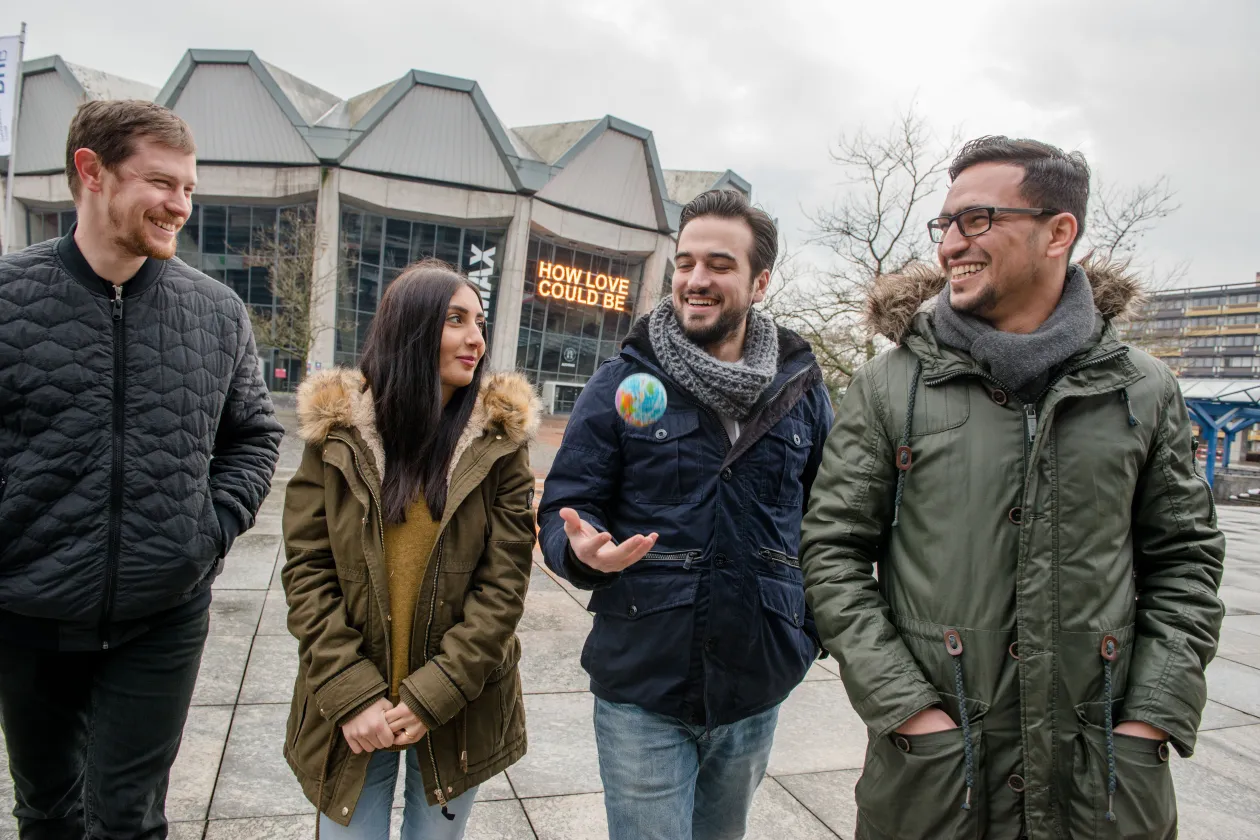Vier Studierende laufen auf dem Campus vor dem Audimax