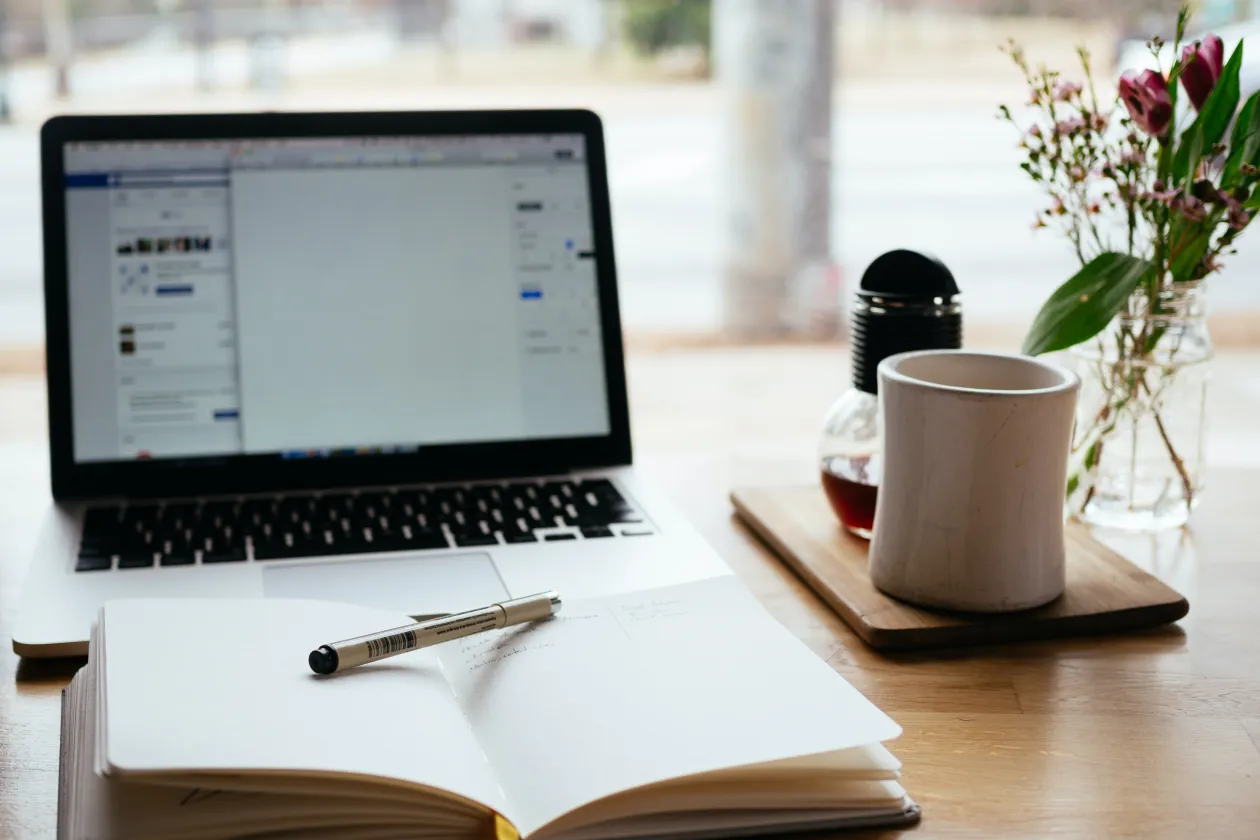 Schreibtisch mit Laptop, Kaffee und Notizbuch
