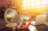 Schreibtisch mit Globus, Laptop und Wörterbüchern