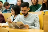 Studierender liest im Hörsaal in einem Heft