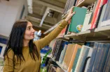 eine Frau zieht ein Buch aus einem Bücherregal in der Bibliothek