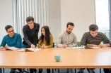 vier geflüchtete Studierende werden beim Lernen bei einer Lehrenden unterstutzt 