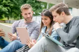 Drei Studierende schauen sich Inhalte auf einem Tablet an.