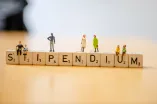 Minifiguren (Little People) sitzen auf dem Scarbble-Schriftzug Stipendien