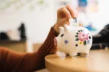 Hand steckt einen Geldschein in ein Sparschwein
