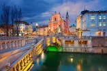 Eine gelb beleuchtete Brücke, die zu einer pinken Kirche in Ljubljana hinführt.