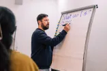 A man writing something on a whiteboard under the Headline "What can i do" at the Working Group Sessions