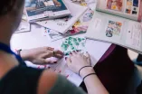A back view picture of a person who is collaging on a table full of magazines.