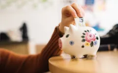 Hand steckt einen Geldschein in ein Sparschwein