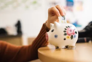 Hand steckt einen Geldschein in ein Sparschwein