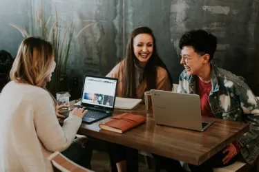 Studierende lachend mit Laptops am Tisch