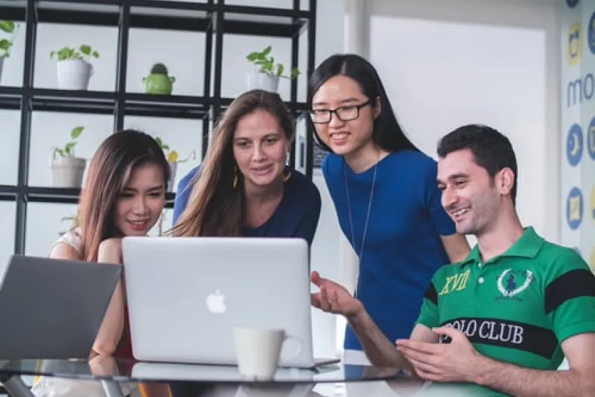 Vier Studierende am Tisch schauen auf Laptop