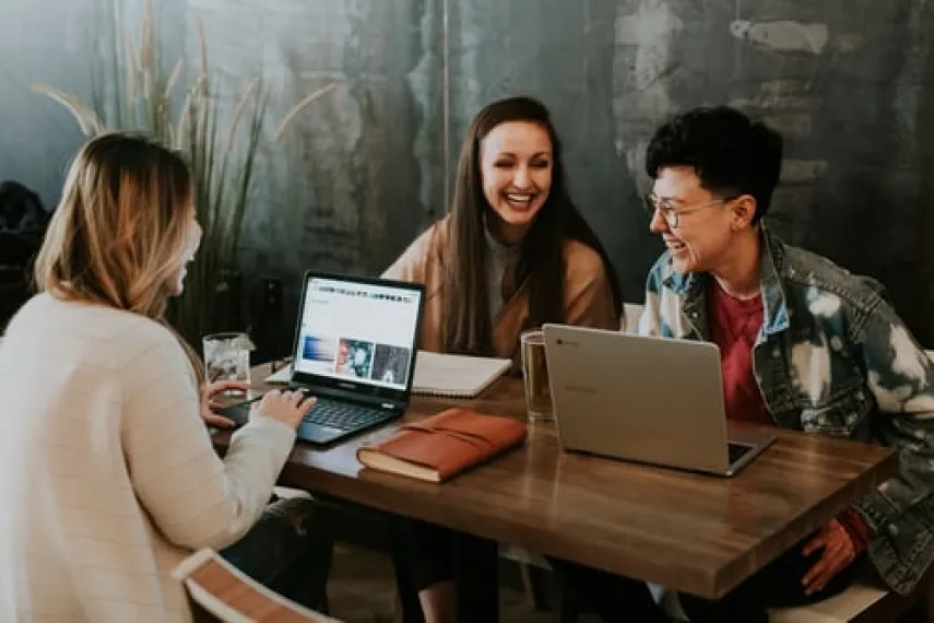 Studierende lachend mit Laptops am Tisch