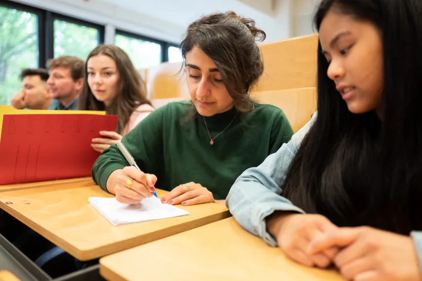 Studierende sitzt im Hörsaal und schreibt mit
