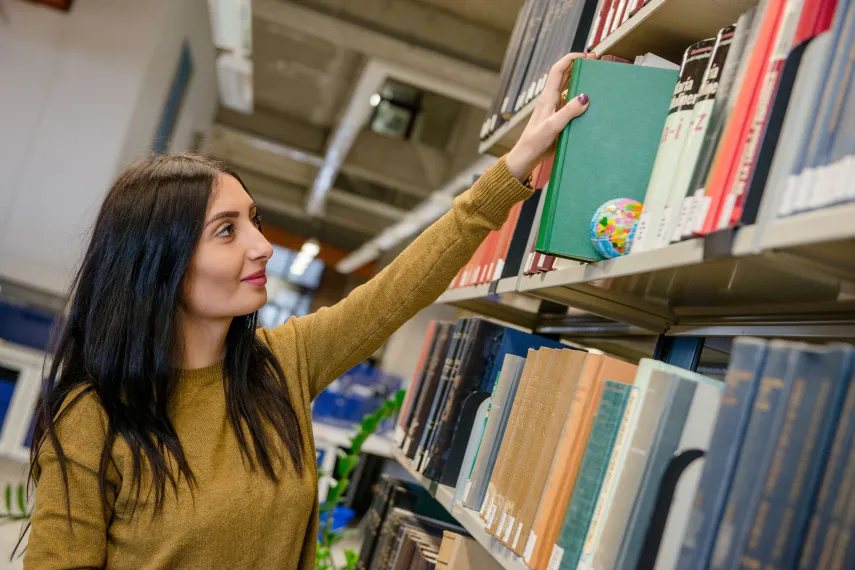 eine Frau zieht ein Buch aus einem Bücherregal in der Bibliothek