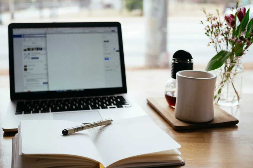 Schreibtisch mit Laptop, Kaffee und Notizbuch