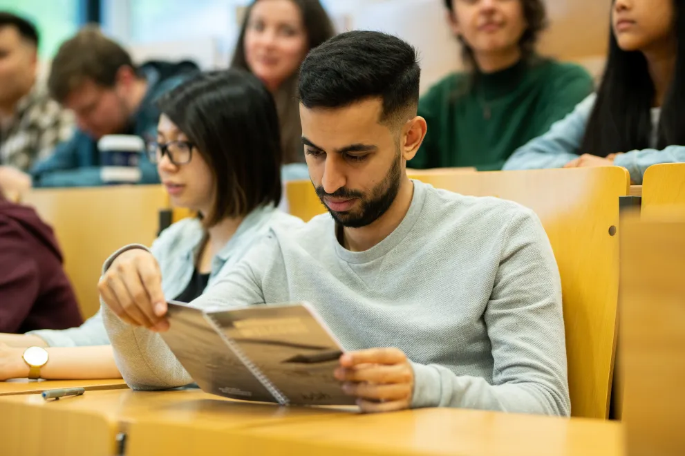 Studierender liest im Hörsaal in einem Heft