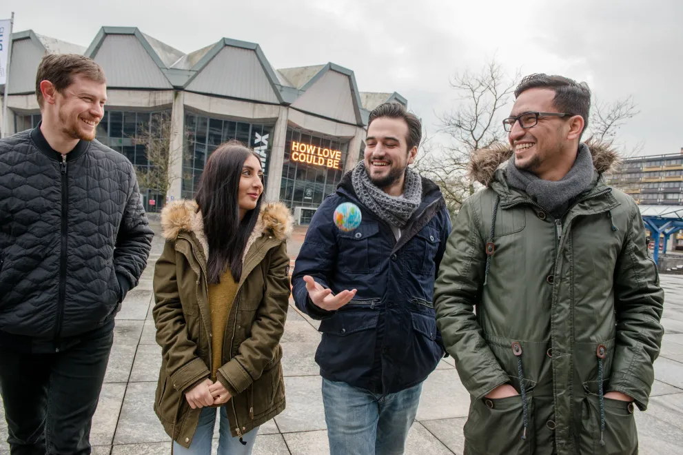 Vier Studierende laufen auf dem Campus vor dem Audimax