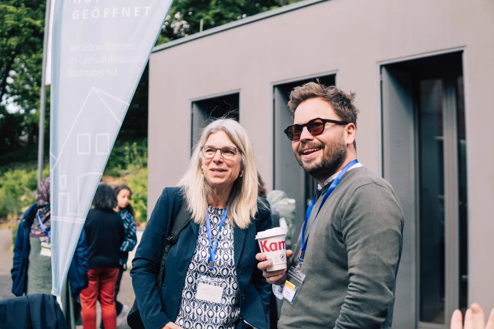 Two Panelists speaking to another at a coffee break, one has a coffee mug in his hand