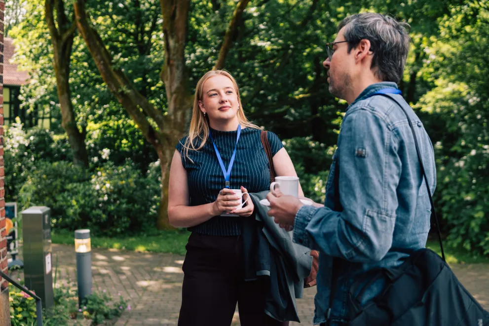 Participants of the Academic Freedom Forum speaking to each other during a coffee break in the Botanical Garden, coffee mugs in hand